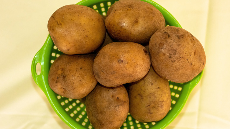 A stack of potatoes in a green basket.