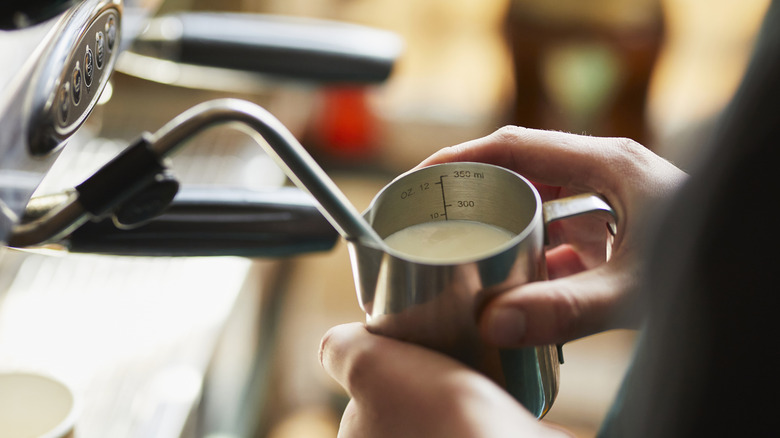 A barista holding a milk jug to a steam wand.