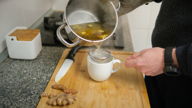 Person pouring turmeric tea through a tea strainer