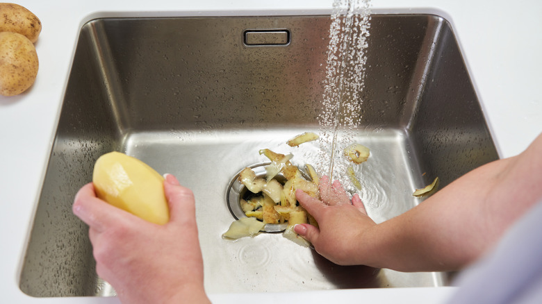 Person holding a potato over a sink and putting peels down the drain