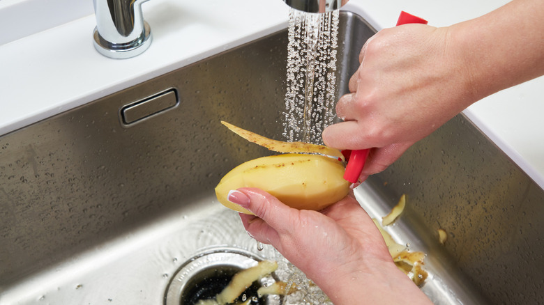 A woman peeling a potato over a sink.