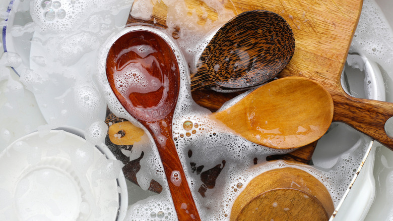 Wooden spoons soaked in soapy water in a sink.