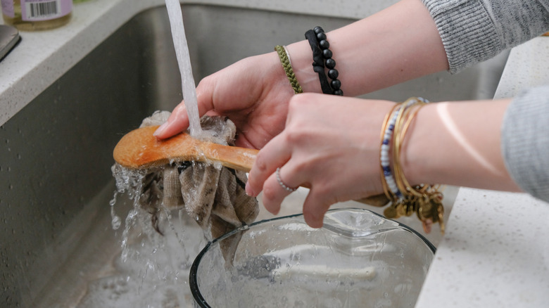person washing a wooden spoon with a sponge under running tap water