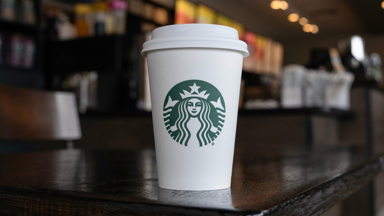 A Starbucks cup for hot beverages sitting on a wooden tabletop.