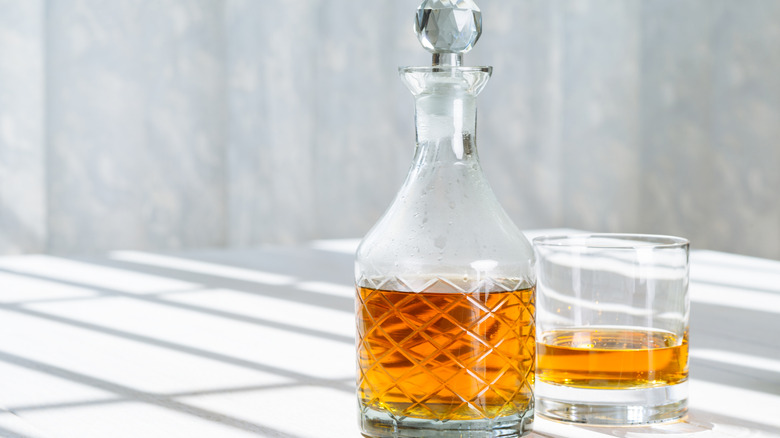 A decanter and a glass of Scotch whisky on a table in direct sunlight from nearby window.