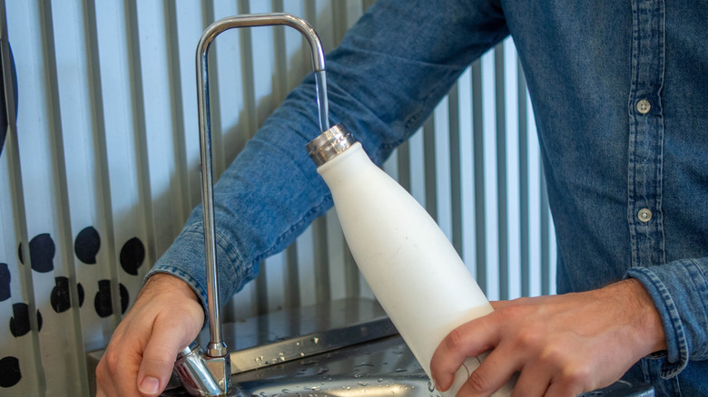 A person's hands are seen filling a reusable bottle at a water filling station.