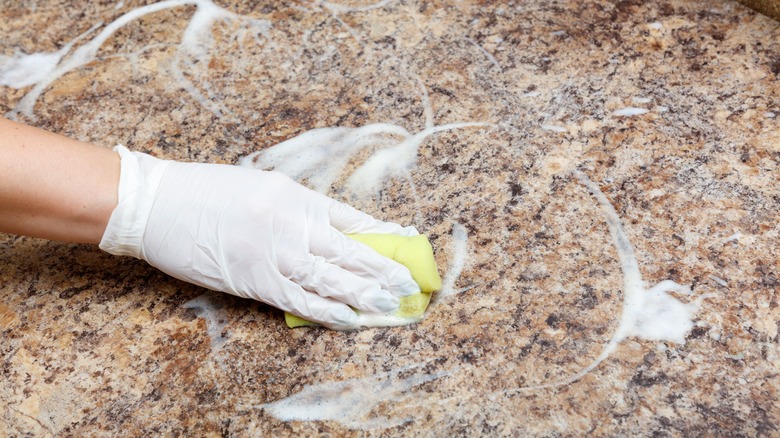 A hand using a sponge and soap to clean a granite countertop