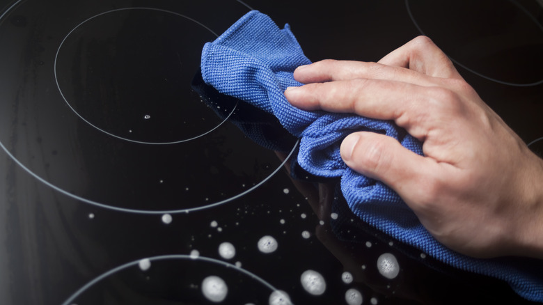 Person cleaning a glass cooktop with sprayed-on cleaner and a microfiber cloth