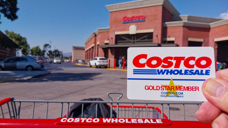 Person holding up Costco membership card outside of a Costco storefront