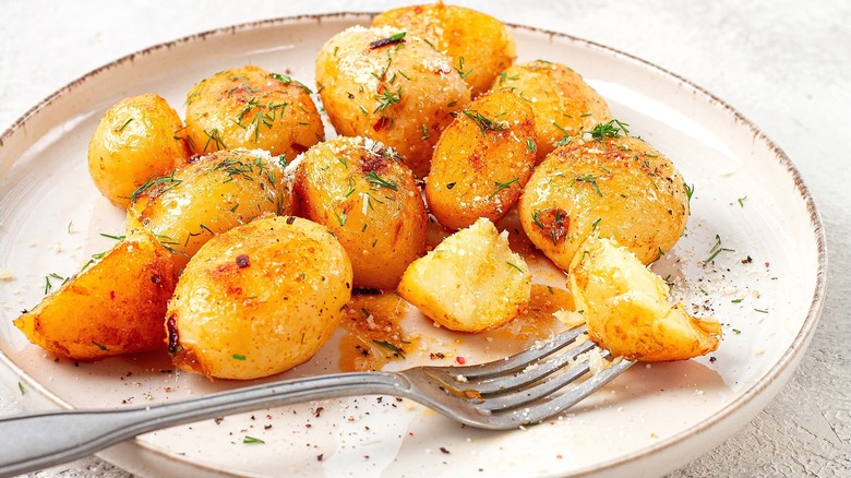 Roasted whole small gold potatoes with salt and dried herbs on a ceramic plate with a metal fork.