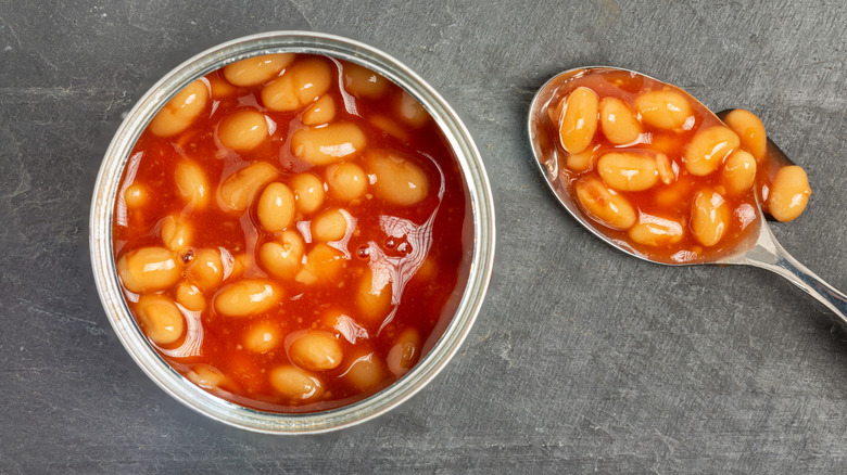 An open can of baked beans sits next to a spoon