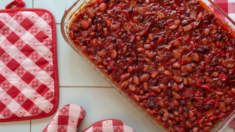 baked beans in a tray, with oven mitts and potholders on the side