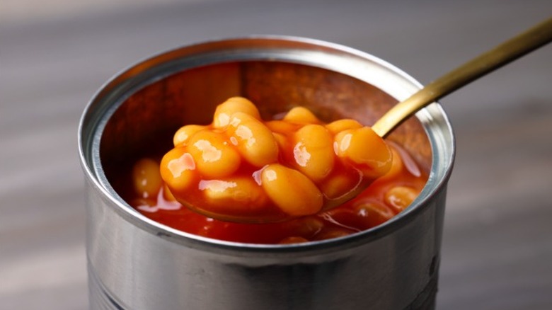 A spoon full of beans being lifted out of a freshly opened can of beans.