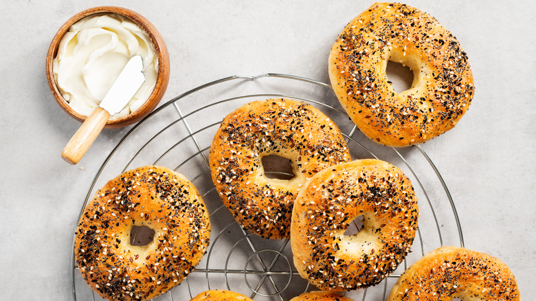 Homemade everything bagels on a round wire cooling rack next to a bowl of cream cheese with a knife
