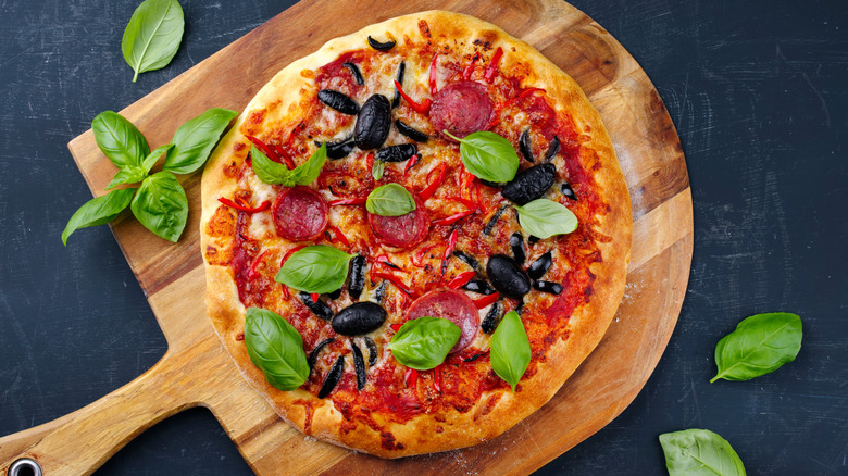 Pizza with pepperoni, chili peppers, black olives, and spinach on a wooden board