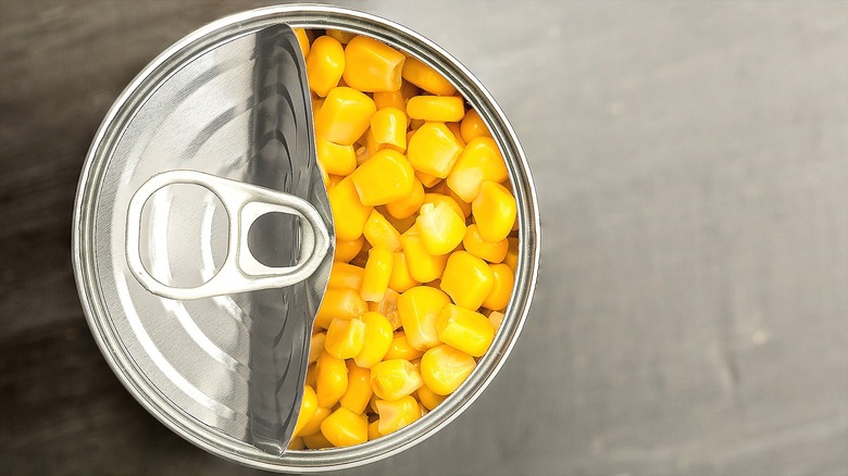 Top-down view of a half-open can of yellow corn over a gray background