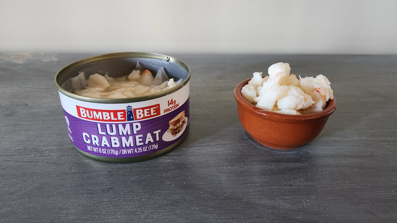 Bumble Bee crabmeat in a can and in a small bowl sit on a gray wooden table.