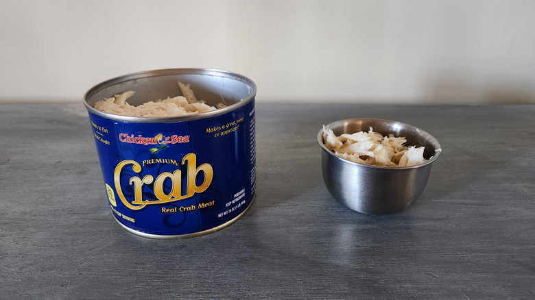 Chicken Of The Sea crabmeat in a can and in a small bowl sit on a gray wooden table.