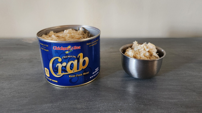 Chicken Of The Sea crabmeat in a can and in a small bowl sit on a gray wooden table.