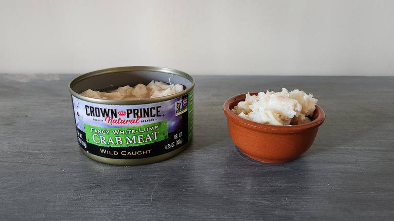 Crown Prince crabmeat in a can and in a small bowl sit on a gray wooden table.