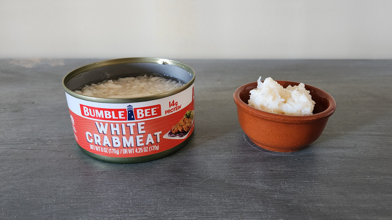 Bumble Bee white crabmeat in a can and in a small bowl sit on a blue wooden table.