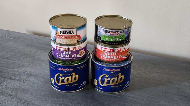 Six cans of crabmeat are arranged on a tabletop.