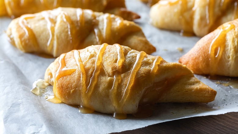 Close-up of apple-stuffed crescent rolls with caramel drizzle on a piece of parchment paper