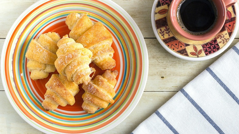 Top-down view of crescent rolls topped with cinnamon-sugar on a multi-colored plate next to a cup of black coffee