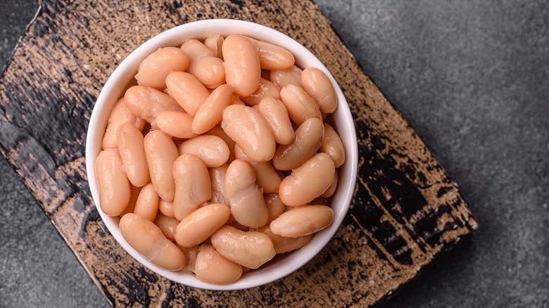 Canned white beans in a white bowl on top of a distressed wooden serving board