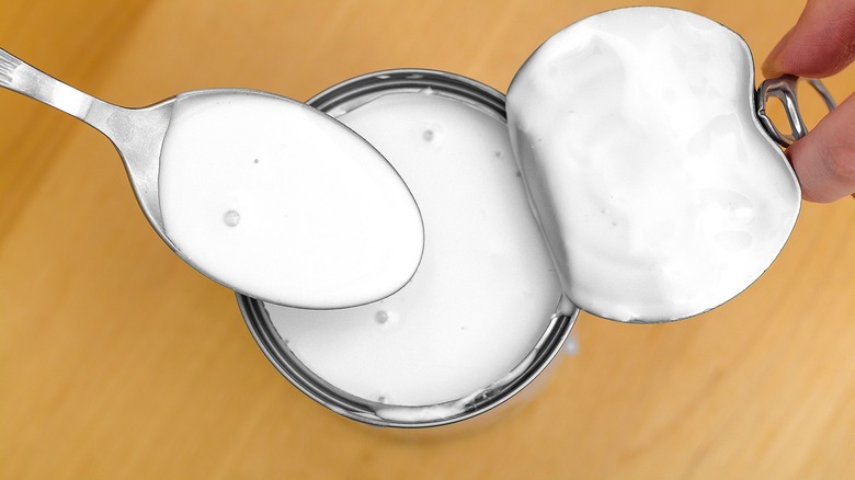 Top-down view of fingers pulling back the lid on a can of coconut milk
