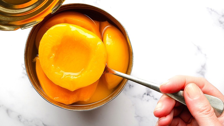 Hand removing halved peaches from a can with a metal spoon