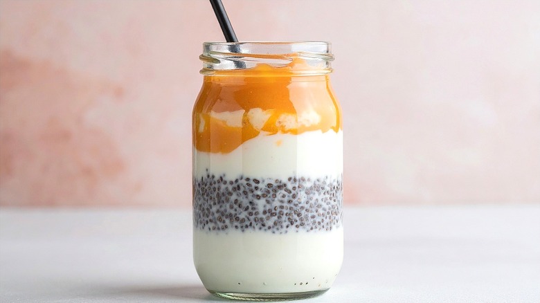 A layered smoothie with apple compote in a glass jar with a black straw