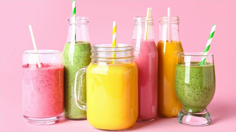 Yellow, pink, and green smoothies in clear glasses with striped straws over a pink background