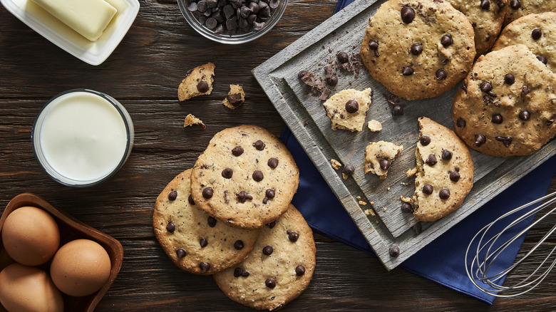 Chocolate chip cookies on a tray and wooden table with ingredients.