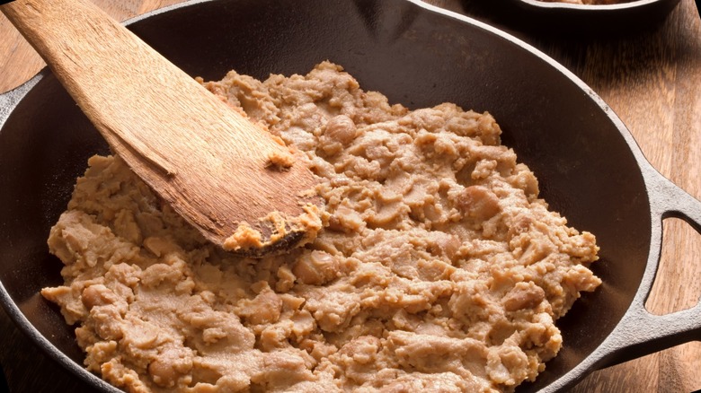 Refried beans are in skillet with a wooden spoon