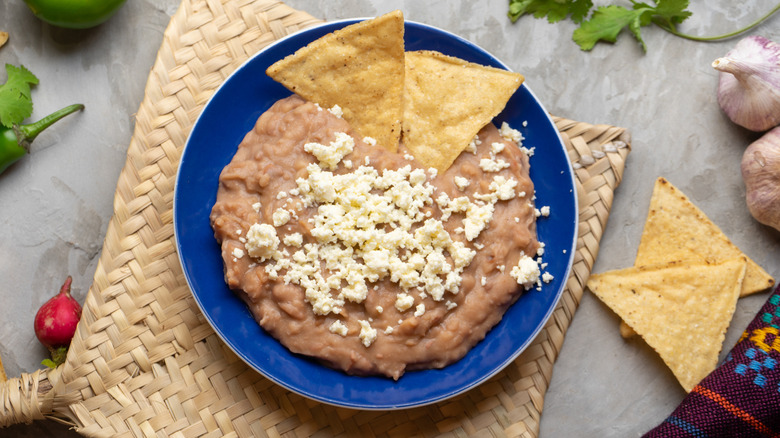 A bowl of refried beans garnished with cheese and served with tortilla chips