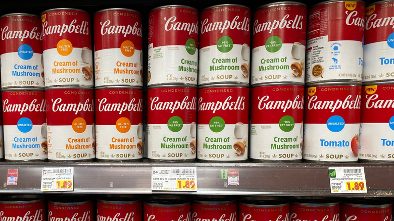 A grocery store shelf featuring multiple cans of Campbell's condensed soups, Cream of Mushroom a the center