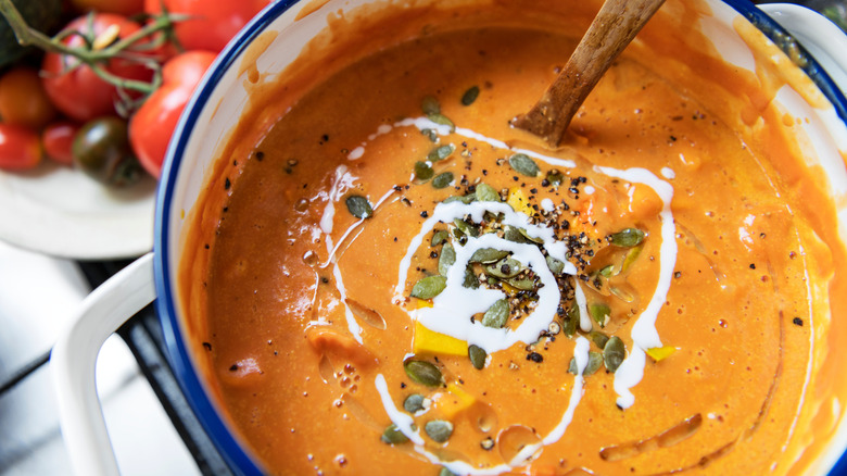 A pot of tomato soup that has been garnished with a swirl of cream