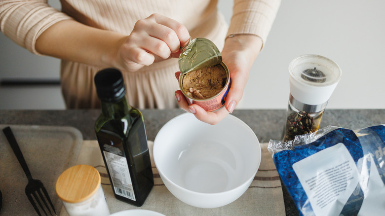 Person opening a can of tuna with other ingredients