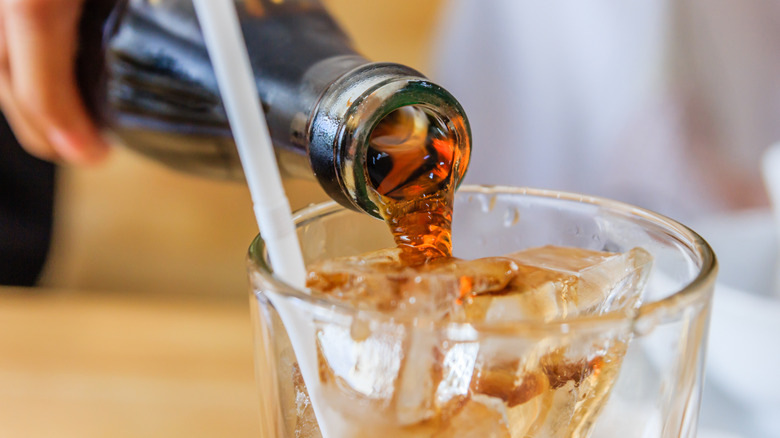 Close up of a glass soda bottle being poured into cup with a straw.