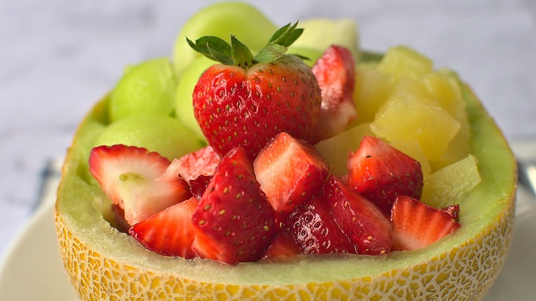 Hollowed-out half of a Galia melon filled with chunks of Galia, honeydew melon, and strawberries