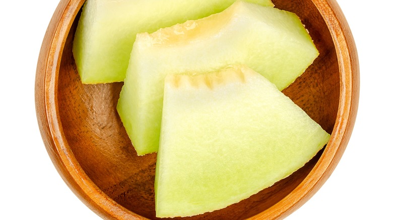 Three chunks of Galia melon in a wooden bowl on a white background