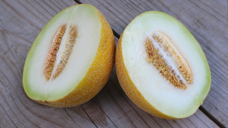 Galia melon cut in half with interior facing front, both on wood table
