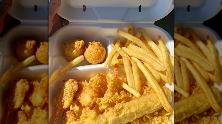 Styrofoam container with fried chicken, fish, hush puppies, and fries