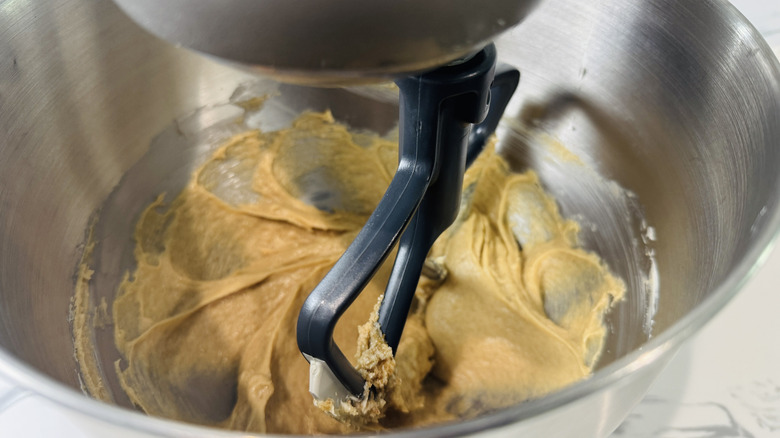 closeup of paddle attachment beating cookie dough in stand mixer bowl