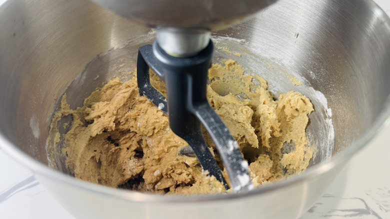 Closeup of paddle attachment beating cookie dough in stand mixer bowl
