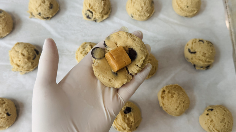 gloved hand holding flattened cookie dough with caramel candy in the center