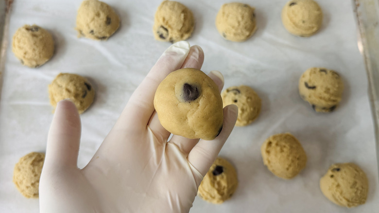 stuffed cookie dough ball in gloved hand with tray of unbaked cookies in the background
