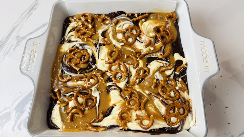 Brownie batter topped with cream cheese and caramel swirls and pretzels