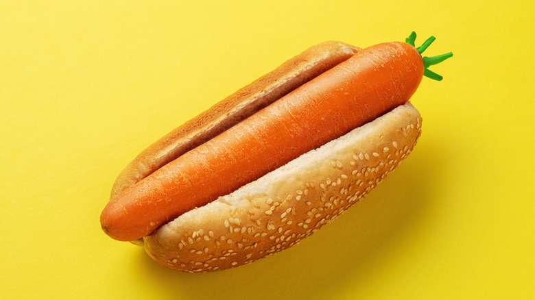 An illustrative image showing a carrot in a hot dog bun on a yellow background.